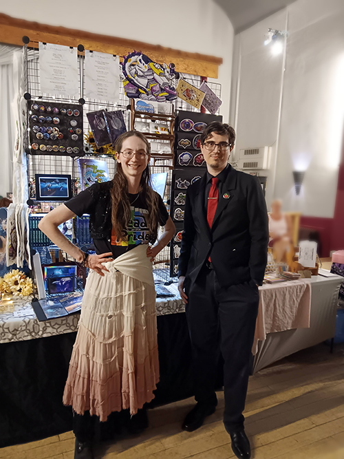 Stephanie and Isaac stand in front of their booth at the Hancock Pride Market.